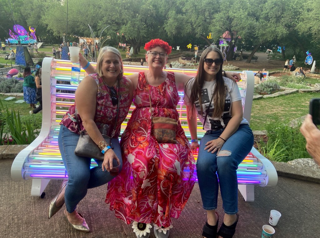 three women sitting in a large garden on a neon bench