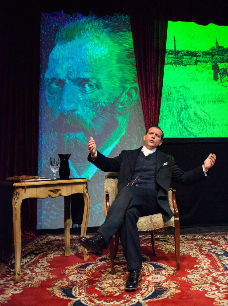 Man sitti g in chair on small stage with image of Van Gogh painting in background